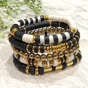 May include: A set of five bracelets featuring black, white, and gold beads. The bracelets are stacked on top of each other, creating a layered look.