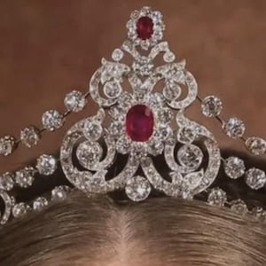 Könnte beinhalten: Ein silberfarbenes Diadem mit komplizierten Schnörkeln und zahlreichen klaren, rund geschliffenen Steinen. Das Stück ist mit fünf markanten, ovalen roten Steinen in der Mitte und an den Seiten sowie mit zarten Steinketten verziert.