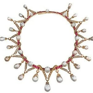 May include: A gold-toned necklace with a series of teardrop-shaped pearls suspended from a red and gold chain. The necklace features small diamonds and red gemstones, creating a delicate and ornate design. The necklace is set against a white background.