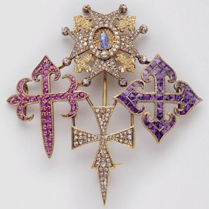 Op de afbeelding: Een gouden broche met drie kruisen en een ster. De kruisen zijn bezet met robijnen, amethisten en diamanten. De ster is bezet met diamanten en heeft in het midden een klein emaillebeeld van de Maagd Maria.