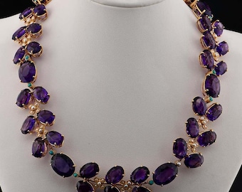 Puede incluir: Un collar de oro con un diseño de piedras preciosas de amatista y esmeralda púrpura. El collar está hecho de amatistas de forma ovalada con pequeños acentos de esmeralda.
