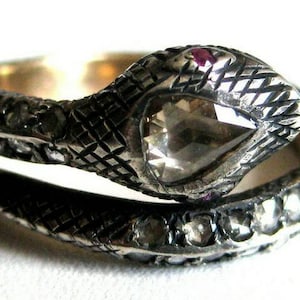 May include: A silver snake ring featuring a large, faceted, brown gemstone and smaller diamonds set in the band. The snake's head is raised and the tail wraps around the finger.