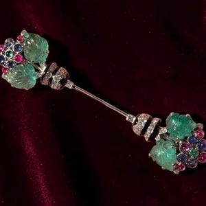 Könnte beinhalten: Eine zweiseitige Brosche mit zwei Clustern aus geschnitzten hellgrünen Blättern, akzentuiert durch kleine runde blaue und rosa Edelsteine. Der Mittelsteg und die Fassungen bestehen aus silberfarbenem Metall mit kleinen klaren Steinen.