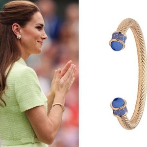 May include: A gold bangle bracelet with blue enamel accents. The bracelet is made of a woven metal design.