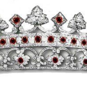 Könnte beinhalten: Ein silberfarbenes Diadem mit geschwungenem Design, verziert mit zahlreichen klaren Edelsteinen und kleinen, runden roten Steinen. Das Diadem hat ein sich wiederholendes Blumenmuster am Sockel, vor weißem Hintergrund.