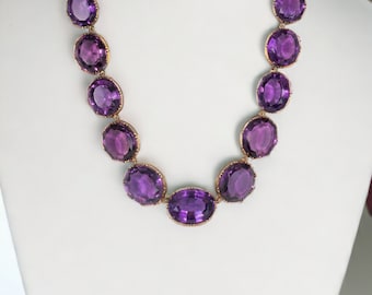 May include: A purple amethyst gemstone necklace with oval-shaped stones set in gold.