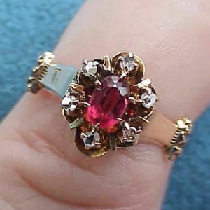 May include: A gold ring with a red oval gemstone surrounded by smaller white gemstones.
