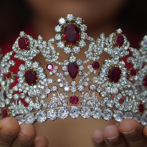 Peut inclure: Une couronne argentée avec des pierres précieuses rouges sur un fond blanc.