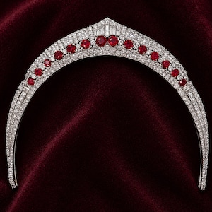 May include: A diamond tiara with a curved design, featuring a row of vibrant red gemstones and numerous smaller diamonds. The tiara is set against a deep red velvet background, showcasing its elegant and luxurious appearance.
