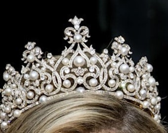 May include: A silver and pearl tiara with a delicate floral design. The tiara is adorned with a row of pearls along the bottom edge and smaller pearls throughout the design.