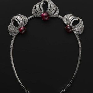 Puede incluir: Una diadema plateada con tres acentos de piedras preciosas rojas y un diseño delicado e intrincado.