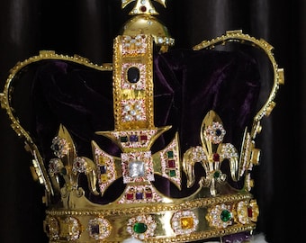 Könnte beinhalten: Eine goldene Krone mit einem violetten Samtbezug und einem Kreuz oben. Die Krone ist mit Juwelen und Perlen verziert.