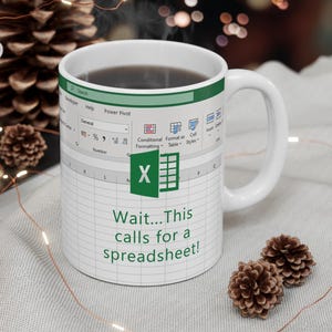 Può includere: Tazza in ceramica bianca con un design a foglio di calcolo e la scritta "Wait...This calls for a spreadsheet!". La tazza presenta un'icona verde di Excel e un motivo a griglia di foglio di calcolo.