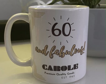 Może przedstawiać: Biały kubek ceramiczny z złotą obwódką i tekstem "60 and fabulous! CAROLE Premium Quality Goods EST. 1963"