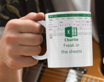 Könnte beinhalten: Weiße Kaffeetasse mit einem grünen Microsoft Excel-Tabellenblatt-Design. Der Text "Charlie Freak in the sheets" ist auf die Tasse gedruckt.