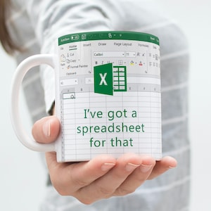 Può includere: Una tazza da caffè bianca con un logo verde di Microsoft Excel e il testo "Ho un foglio di calcolo per questo".