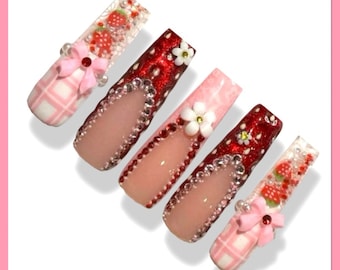 Könnte beinhalten: Fünf lange, rosa und rote künstliche Nägel mit Strasssteinen, Glitzer und kleinen Blumen- und Schleifendekorationen.