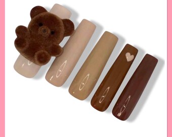 May include: Set of six long, rectangular false nails with a gradient of brown shades. The nails are decorated with a small brown teddy bear on one nail and a small white heart on another nail.