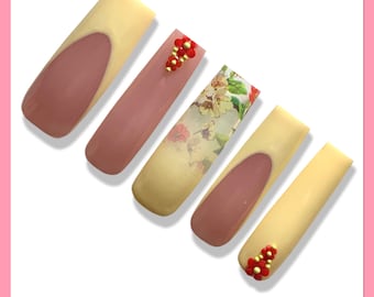 May include: Five long, almond-shaped artificial nails with different designs. One nail has a floral pattern, another has red and gold beads, and the rest are a light yellow with a pink base.