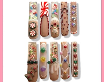 Op de afbeelding: Een set van tien lange, kunstmatige nagels met een kerstthema. Ontwerpen omvatten zuurstokken, peperkoekmannetjes en sprankelende accenten. Kleuren zijn bruin, rood, groen, wit en goud. Elke nagel is uniek versierd met feestelijke details.
