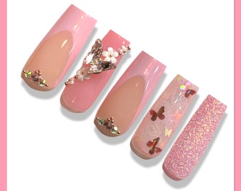 May include: Five pink and white long false nails with different designs. One nail has a butterfly and flower embellishment, another has a butterfly design, and another has glitter.