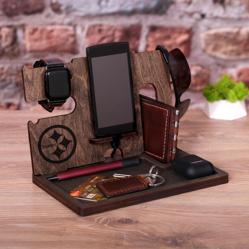 Pu&ograve; includere: Un organizzatore in legno con il logo degli Steelers, slot per un telefono, un orologio e occhiali da sole, e un vassoio per chiavi, carte e altri piccoli oggetti.
