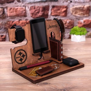 Pu&ograve; includere: Porta telefono in legno con logo Steelers, un porta orologio, uno slot per telefono, un portachiavi, uno slot per portafoglio e uno spazio per un paio di occhiali. Il supporto &egrave; personalizzato con il nome "James".
