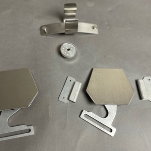 May include: A set of silver metal hardware pieces, including two hexagonal plates with mounting brackets, a small round piece with holes, and two rectangular pieces with holes.