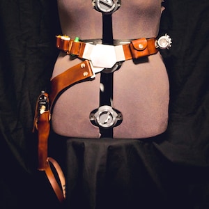 May include: A brown leather belt with a silver buckle and a silver pouch. The belt is worn on a mannequin and has a brown leather holster attached to it.