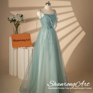 May include: A light blue tulle gown with a sequined bodice and thin straps. The gown has a flowing skirt and is displayed on a mannequin. The text "ShanrongArt Handmade Design Your personal beauty Creator" is visible at the bottom of the image.