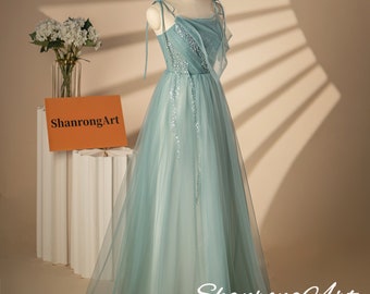 Può includere: Un abito in tulle azzurro chiaro con un corpetto di paillettes e sottili spalline. L'abito ha una gonna fluida ed è esposto su un manichino. Il testo "ShanrongArt Handmade Design Your personal beauty Creator" è visibile nella parte inferiore dell'immagine.