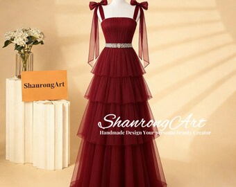 May include: A burgundy tiered formal gown with bow straps and a jeweled belt. The dress is displayed on a mannequin. The text "ShanrongArt Handmade Design Your personal beauty Creator" is visible.