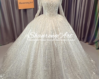 Puede incluir: Un deslumbrante vestido de novia blanco con mangas largas y una falda amplia. El corpiño presenta un intrincado trabajo de abalorios, y el vestido se exhibe en un maniquí. La marca "ShanrongArt" es visible en un letrero.