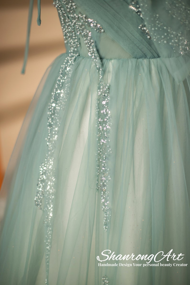 May include: A light blue tulle dress with silver embellishments. The dress has a fitted bodice and a flowing skirt. The skirt is decorated with silver sequins and beads. The dress is perfect for a special occasion.