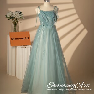 May include: A light blue tulle gown with a sequined bodice and thin straps. The gown has a flowing skirt and is displayed on a mannequin. The text "ShanrongArt Handmade Design Your personal beauty Creator" is at the bottom of the image.