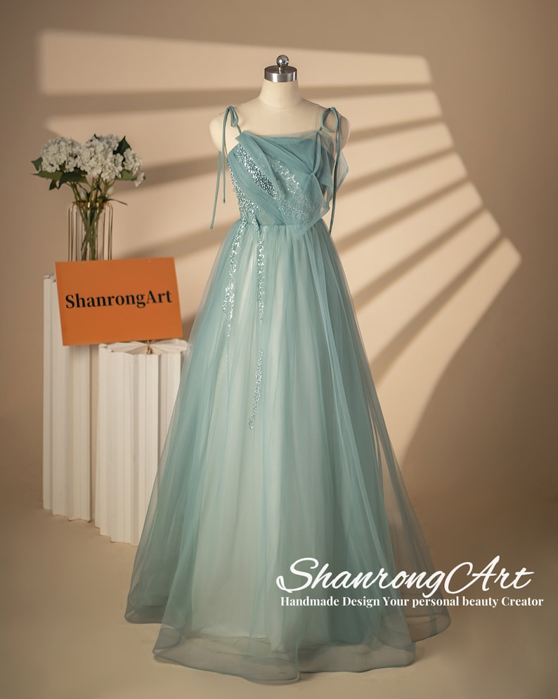 May include: A light blue tulle gown with a sequined bodice and thin straps. The gown has a flowing skirt and is displayed on a mannequin. The text "ShanrongArt Handmade Design Your personal beauty Creator" is at the bottom of the image.
