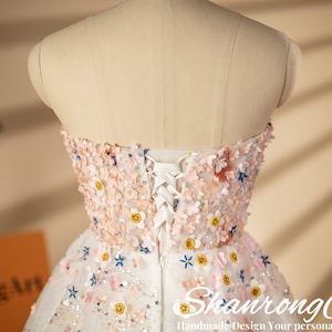 K&ouml;nnte beinhalten: Ein wei&szlig;es tr&auml;gerloses Kleid mit Blumenmuster und einem Schn&uuml;rr&uuml;cken. Das Kleid ist mit rosa, blauen und gelben Blumen verziert.