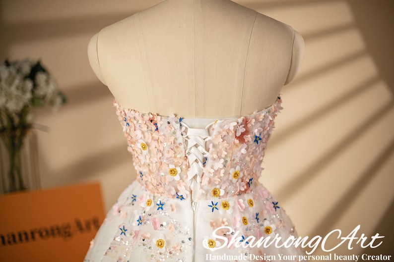 K&ouml;nnte beinhalten: Ein wei&szlig;es tr&auml;gerloses Kleid mit Blumenmuster und einem Schn&uuml;rr&uuml;cken. Das Kleid ist mit rosa, blauen und gelben Blumen verziert.