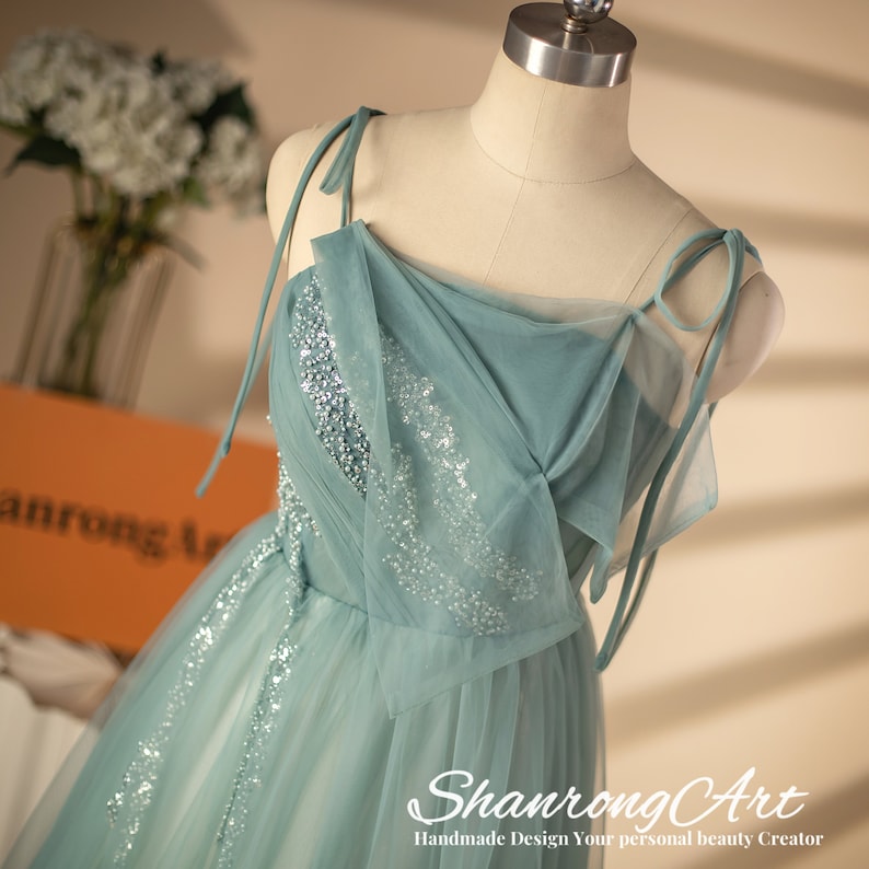 May include: A light blue tulle dress with a beaded bodice and thin straps. The straps tie at the shoulders. The dress has a flowing skirt.