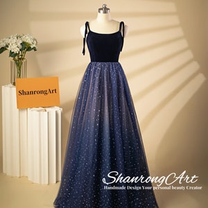 Op de afbeelding: Een donkerblauwe avondjurk van fluweel en tule met een aansluitend lijfje en een volle rok. De rok is versierd met zilveren glittersterren.