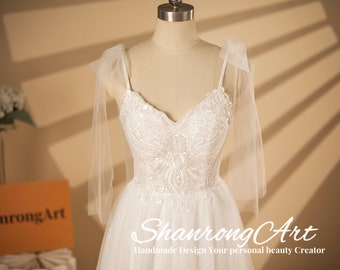 May include: A white tulle wedding dress with a beaded bodice and a sweetheart neckline. The dress has a fitted bodice and a flowing skirt. The dress has a bow on each shoulder strap.