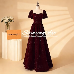 May include: A burgundy velvet gown with a square neckline and short sleeves. The dress has a full skirt and is embellished with subtle sparkling details. The text "Shanrong Art" is visible on the dress. The dress is displayed on a mannequin.