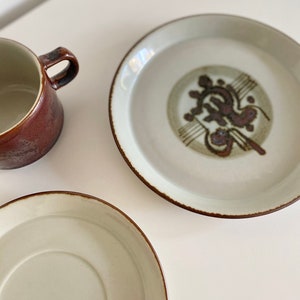 May include: A set of two ceramic plates with a brown rim and a white centre. One plate has a brown and green design in the centre. The other plate is plain.