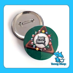 May include: A round button with a green background featuring a pool table design and the text "POOL SHARK". The button has a silver pin back. The image also includes a cartoon cat and the text "Tacey Shop".