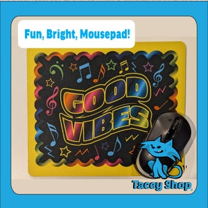 May include: Yellow mousepad with a black background and colorful "Good Vibes" text surrounded by musical notes and stars. A black computer mouse with a blue cartoon cat on top is on the mousepad.