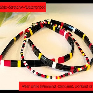 May include: Three colorful beaded bracelets in black, red, white, and yellow. The bracelets are made of square beads and are stacked on top of each other. The text "Comfortable-Stretchy-Waterproof" is at the top of the image. The text "Wear while swimming, exercising, working or playing" is at the bottom of the image.