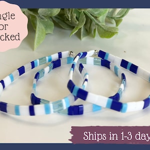 May include: Three blue, white, and light blue tiled bracelets stacked on top of each other. The bracelets are made of glass tiles and have a silver clasp. "Single or Stacked" is written in pink on a white background.