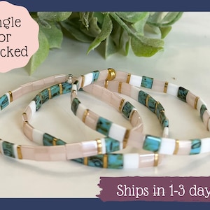 May include: Three beaded bracelets in a stack. The bracelets feature a mix of pink, white, and turquoise rectangular beads, separated by gold-colored accents. The text "Single or Stacked" is in a pink circle, and "Ships in 1-3 days" is in a purple rectangle.