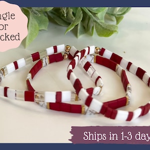 May include: Three stacked bracelets with red and white beads and gold accents. The bracelets are made of ceramic and glass beads.  Single or stacked.