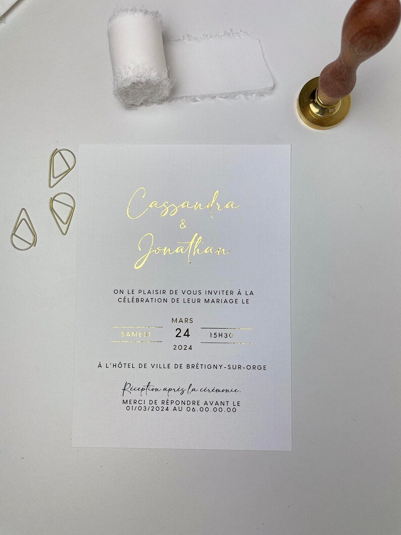 Puede incluir: Una invitaci&oacute;n de boda blanca con letras doradas anunciando el matrimonio de Cassandra y Jonathan. La boda tendr&aacute; lugar el s&aacute;bado 24 de marzo de 2024 a las 3:30 PM en el H&ocirc;tel de Ville de Br&eacute;tigny-sur-Orge. La recepci&oacute;n seguir&aacute; a la ceremonia. Por favor, responda antes del 1 de marzo de 2024.